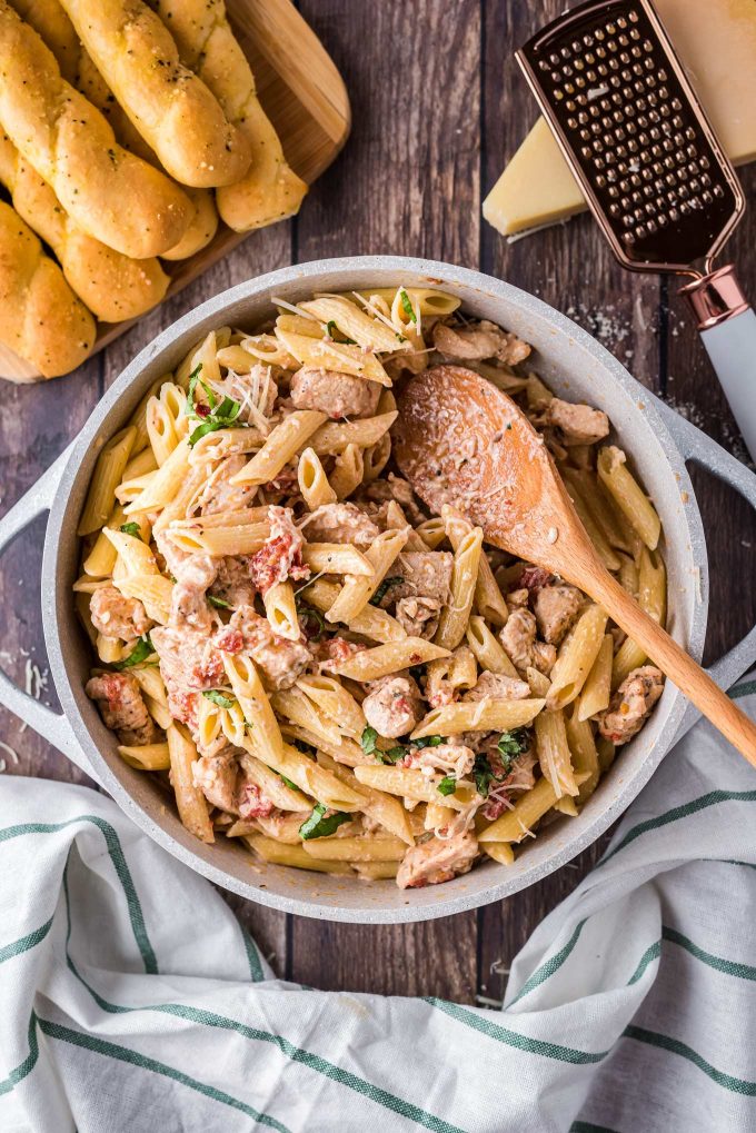 wooden spoon stirring sun dried tomato pasta in pot