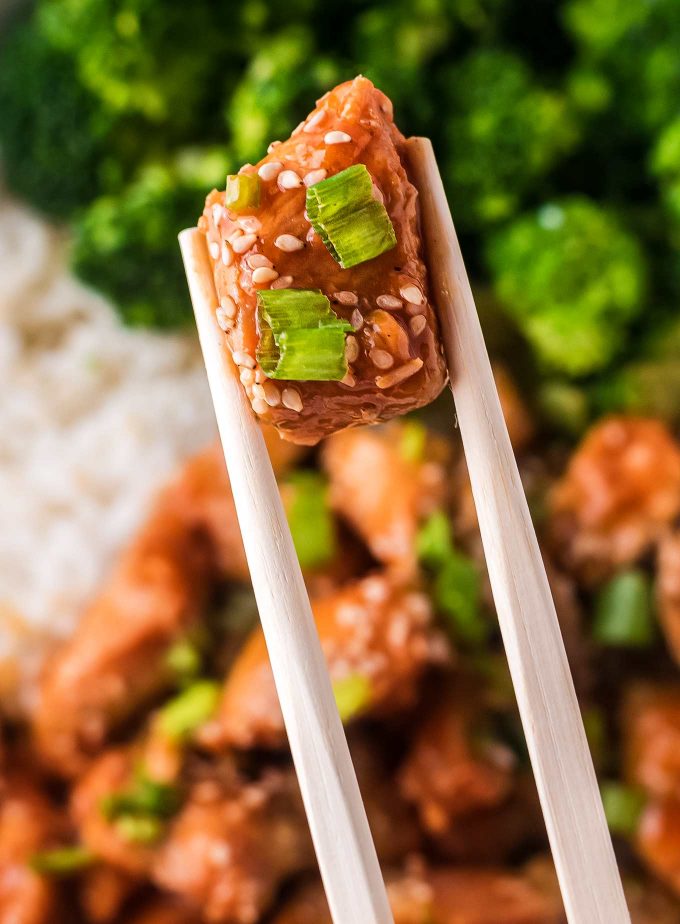 chopsticks holding a piece of chicken with sesame seeds and green onions