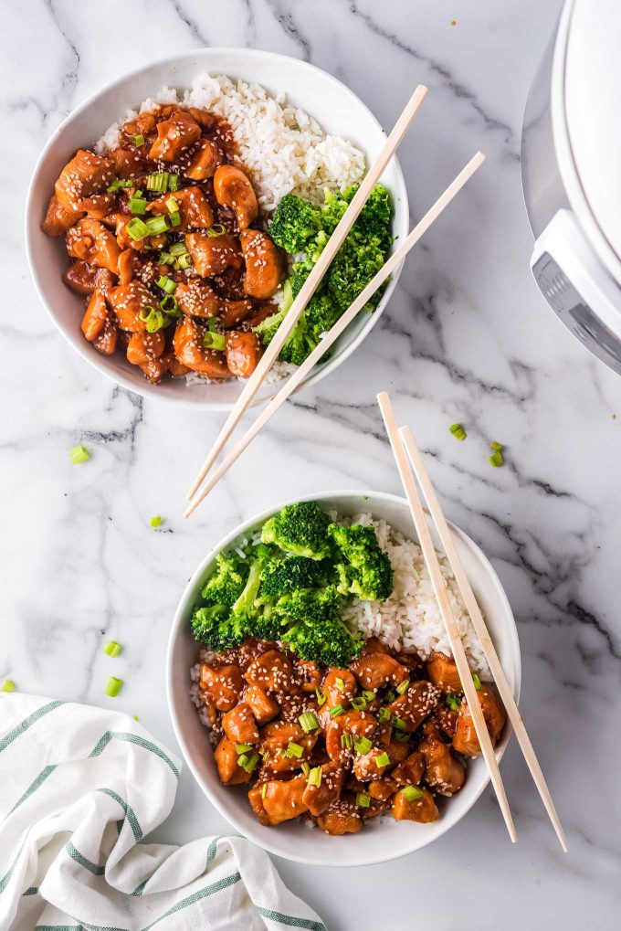 2 bowls with sesame chicken, rice and broccoli with chopsticks