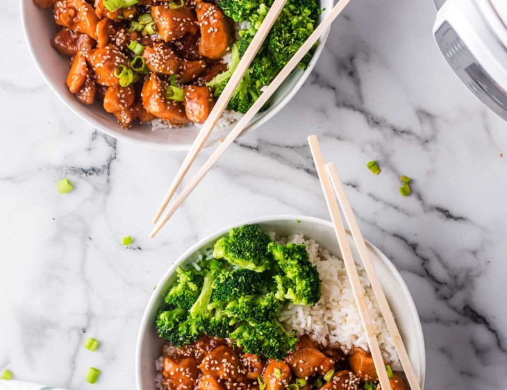2 bowls with sesame chicken, rice and broccoli with chopsticks