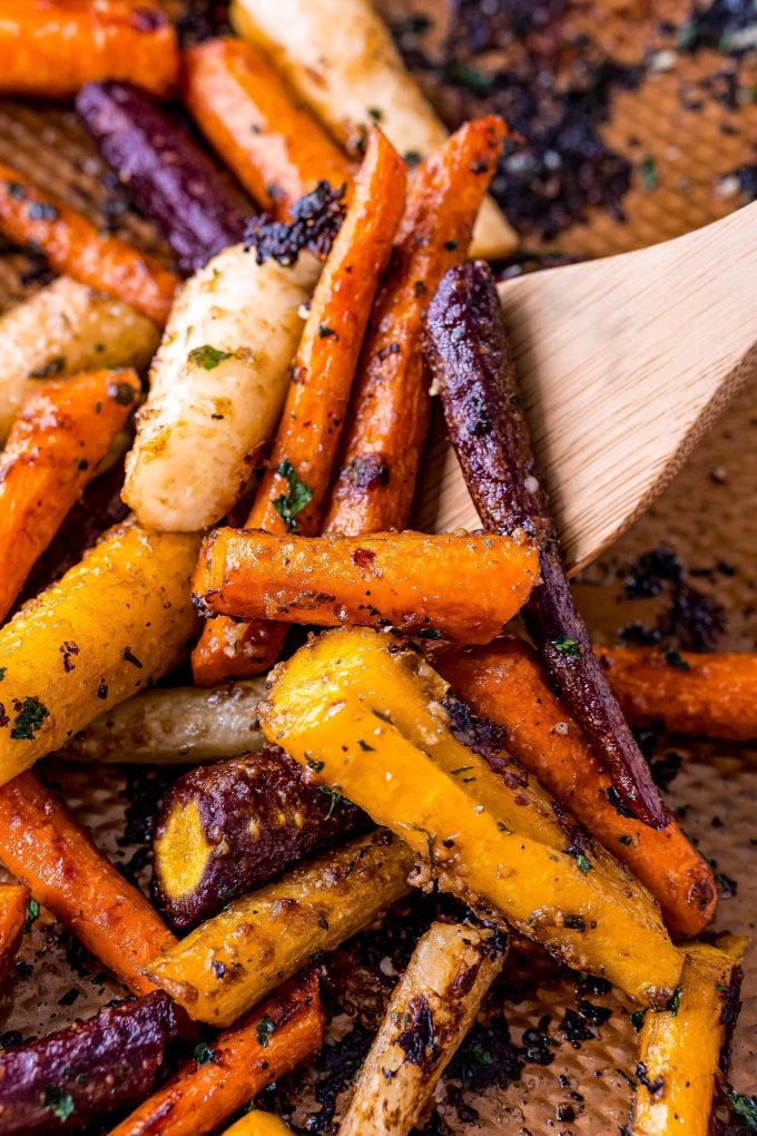 wooden spoon scooping up carrots on baking sheet