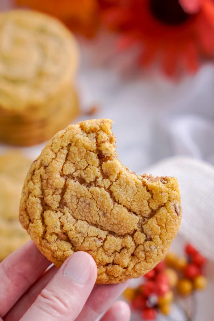 holding up a pumpkin cookie with a bite taken out of it