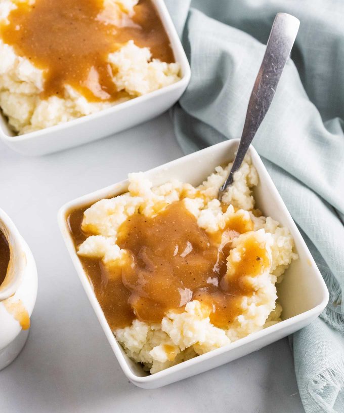 two white dishes of mashed potatoes with gravy