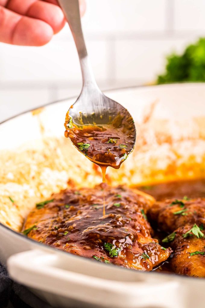 spooning honey garlic sauce over chicken breast in skillet