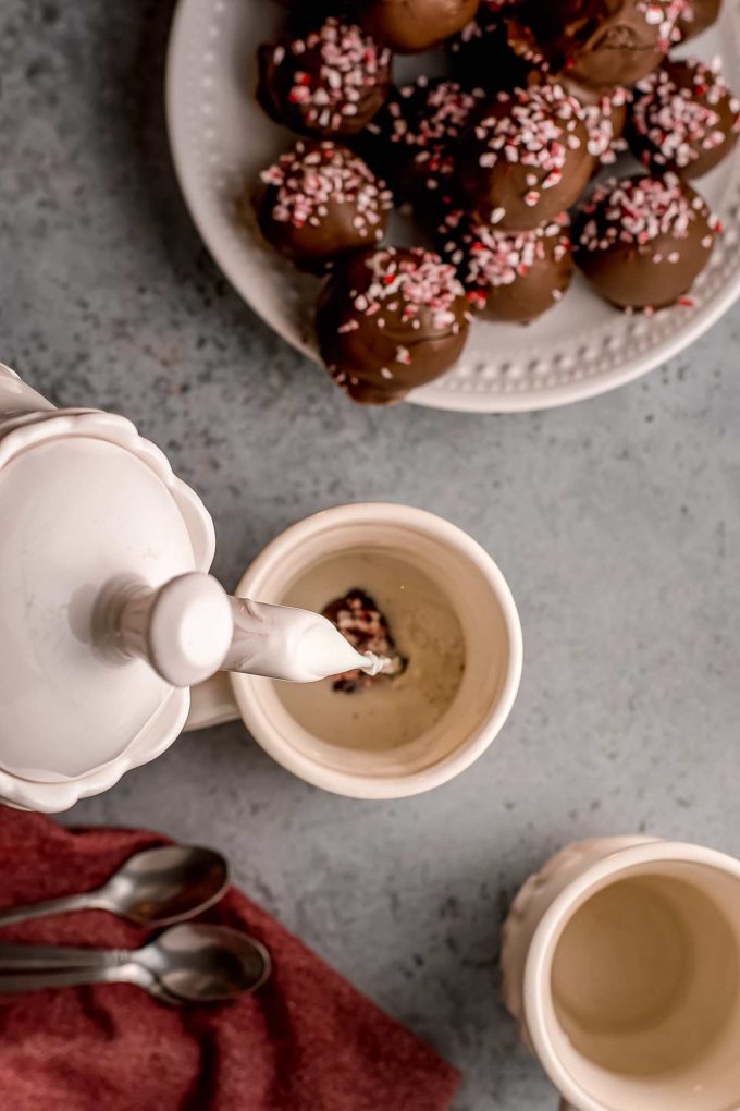 pouring hot milk over a hot chocolate bomb in mug