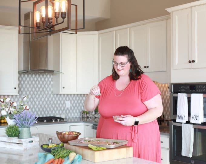 woman sprinkling seasoning on sheet pan of food