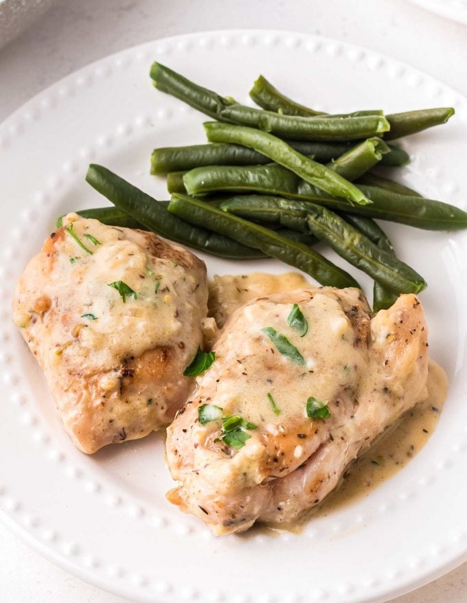 two chicken thighs on plate topped with creamy mustard sauce