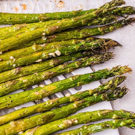using a spatula to pick up roasted asparagus from a baking sheet