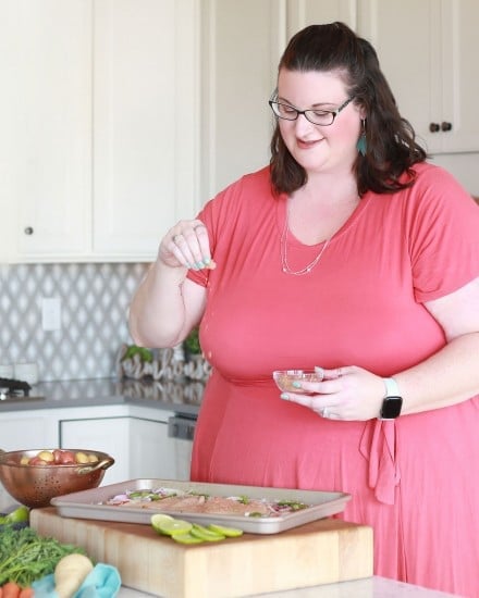 woman seasoning chicken on baking sheet