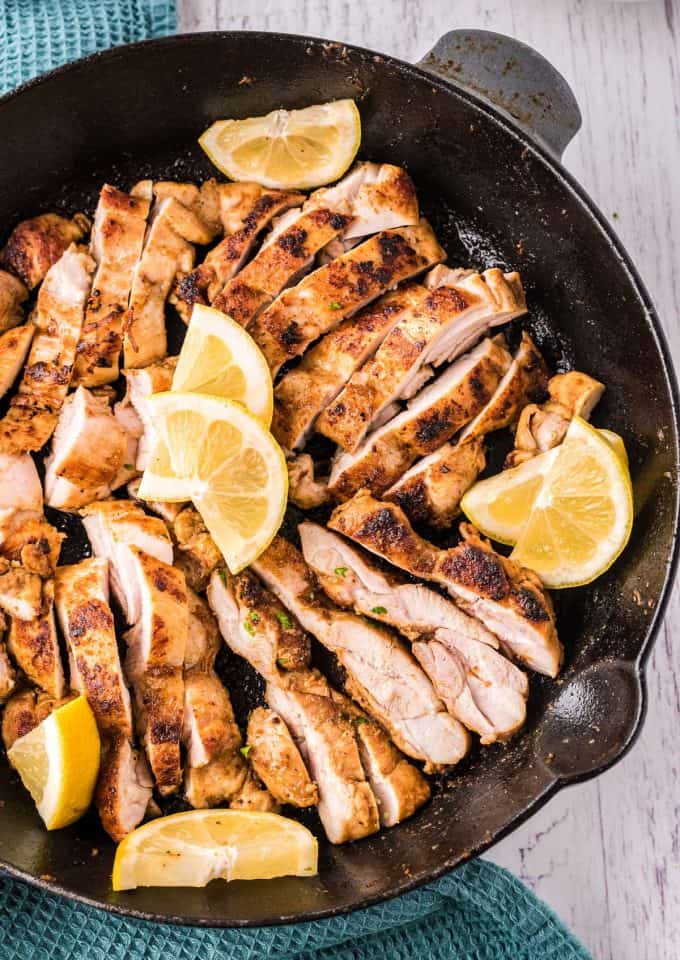 sliced chicken shawarma in cast iron skillet with lemon wedges