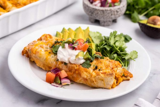 white plate with enchilada, avocado, and cilantro