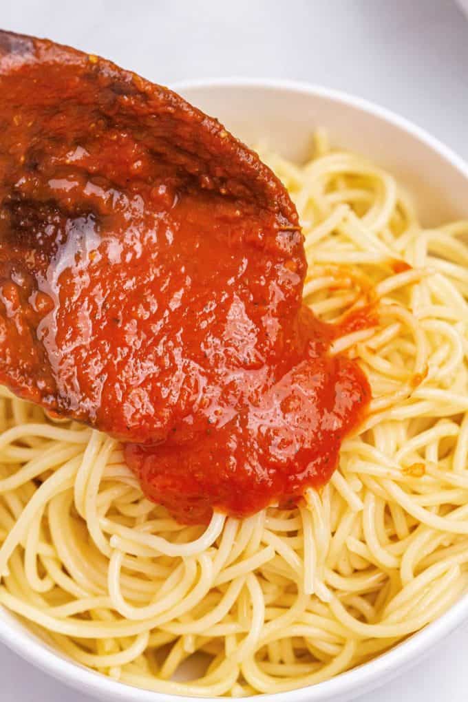 spooning marinara sauce onto pasta