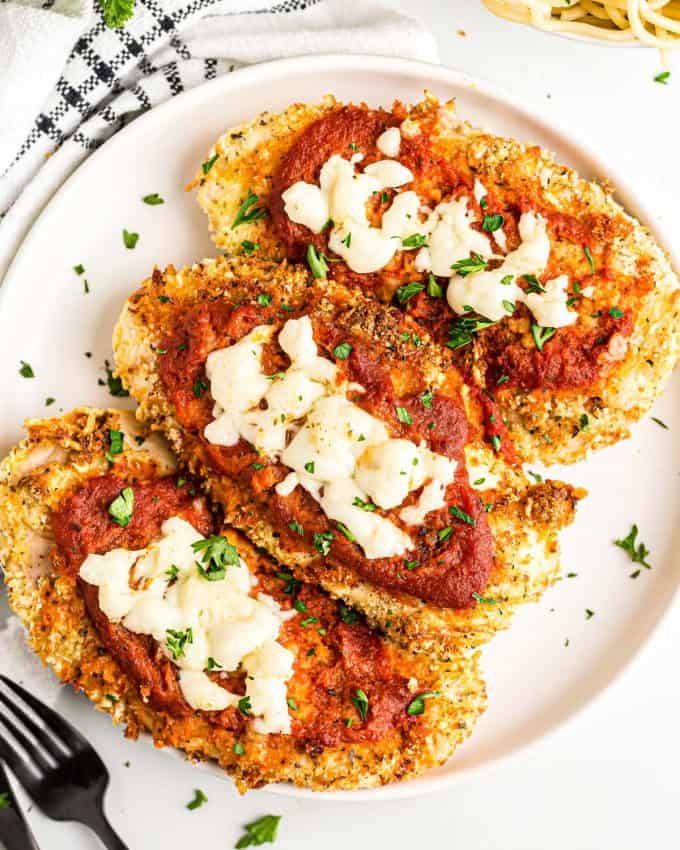 three chicken parmesan breasts on white plate