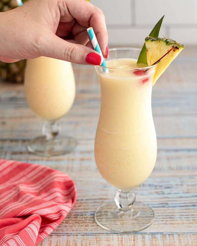 adding a straw to a glass filled with pina colada cocktail