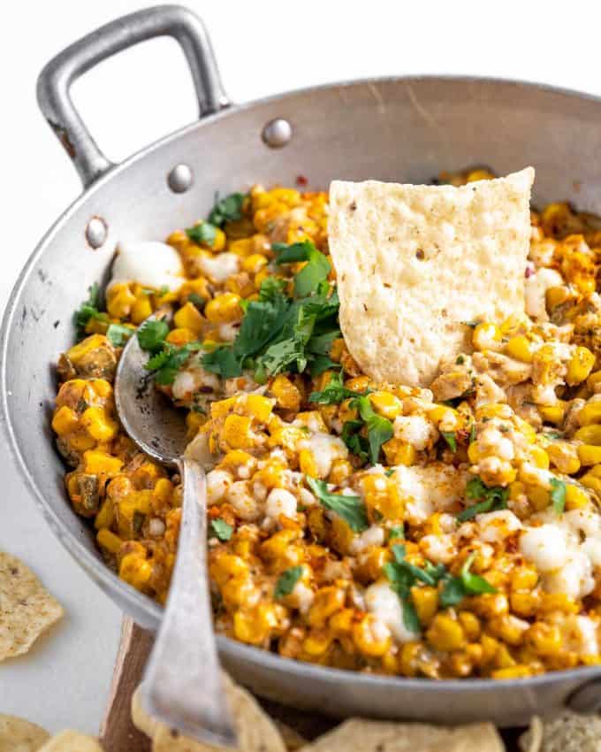 street corn dip in skillet with spoon and chip