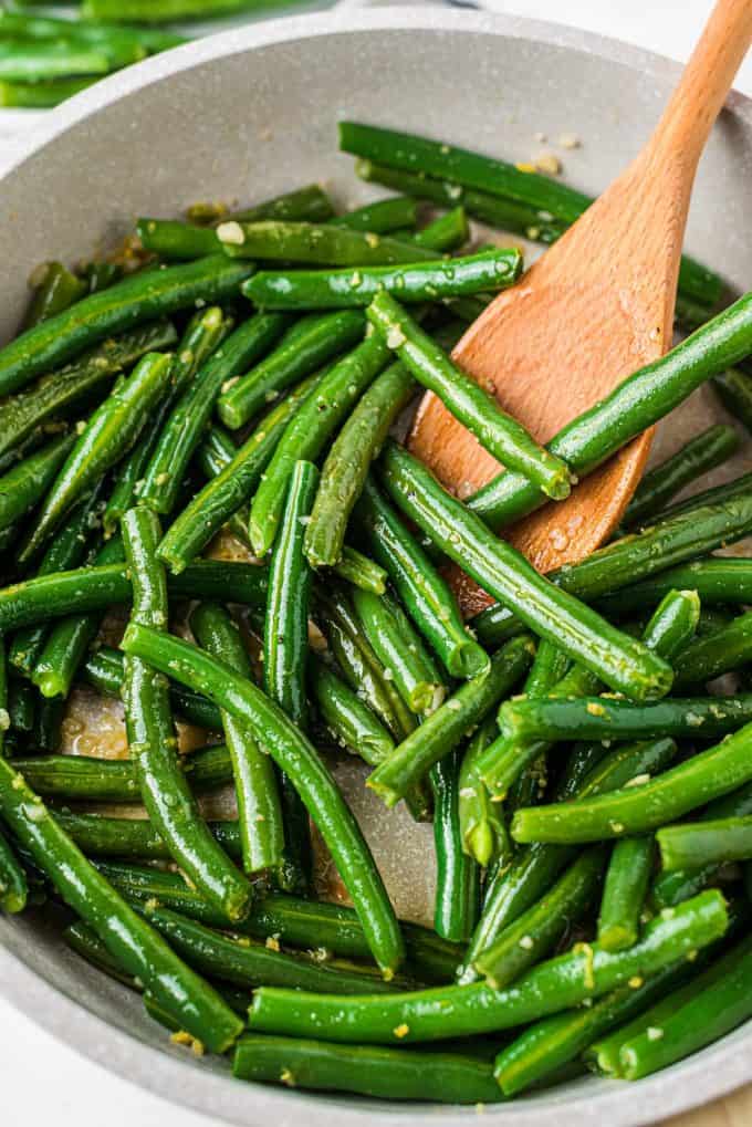 stirring green beans in skillet