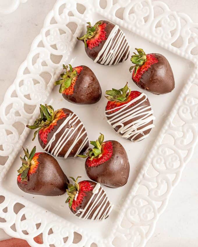 drizzled chocolate covered strawberries on white platter.