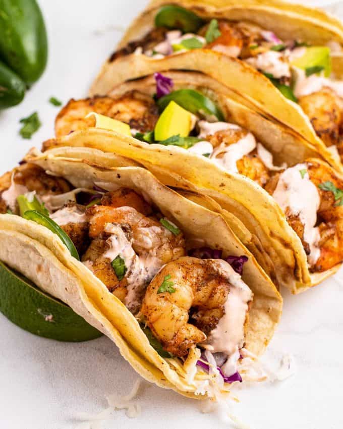 three corn tortilla tacos with grilled shrimp and lime wedges