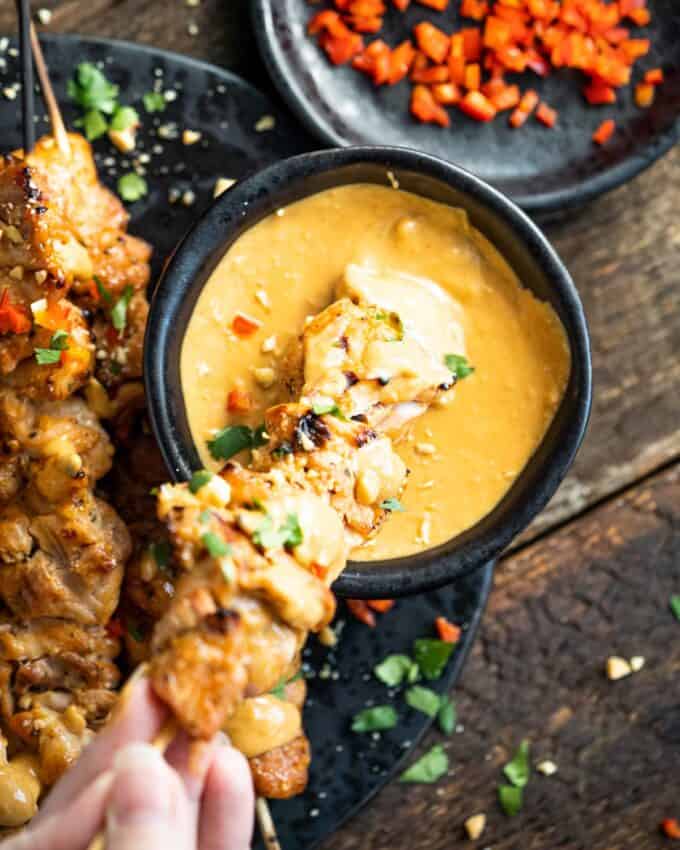 dipping chicken satay skewer into peanut sauce