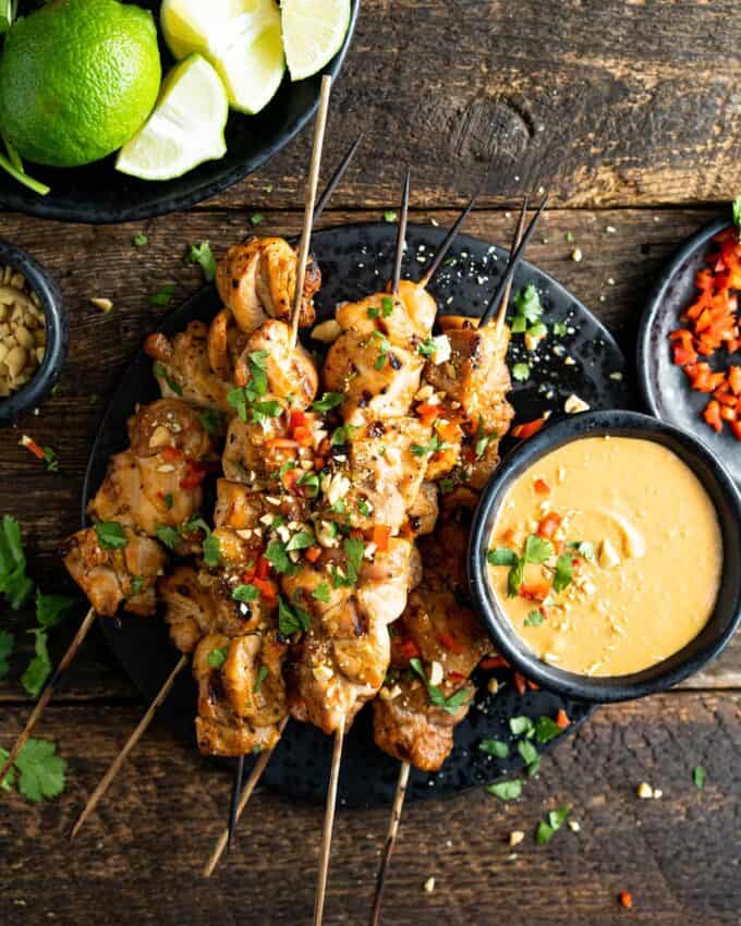 stack of chicken satay skewers on plate with bowl of peanut sauce
