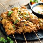 pile of chicken satay skewers on black plate