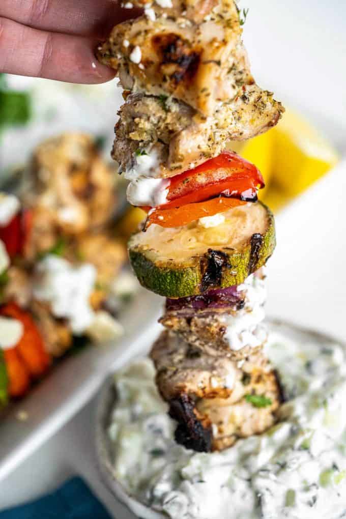 dipping greek chicken kebabs into tzatziki sauce