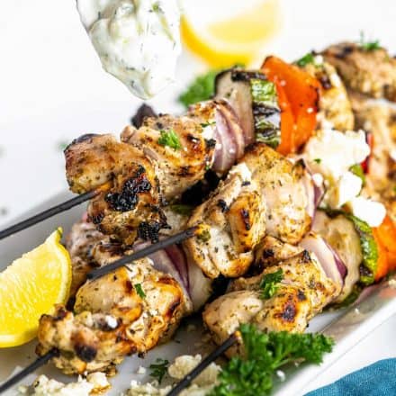 drizzling tzatziki sauce on greek chicken kebabs