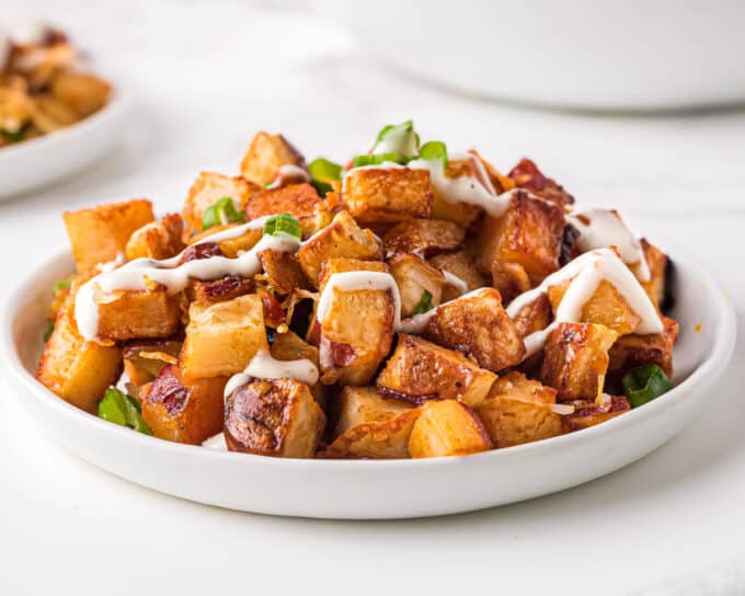 These crispy Cheesy Buffalo Roasted Potatoes are the side dish you never knew you needed in your life! Spiced potatoes, tangy hot sauce, gooey cheese, crispy bacon, fresh green onions... and top it all off with a drizzle of ranch or blue cheese dressing! #sidedish #potatoes #buffalo