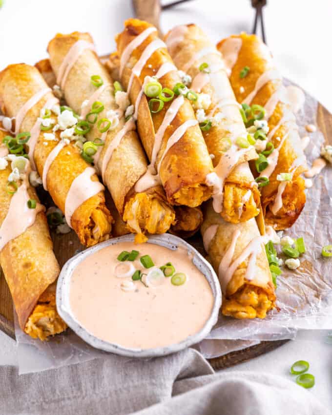 These Buffalo Chicken Taquitos are the perfect crowd-pleasing appetizer! Cheesy buffalo chicken filling is rolled up in flour tortillas and baked until crispy. Serve with an easy buffalo ranch and sprinkled with green onions and blue cheese crumbles! #buffalochicken #taquitos #appetizer #partyfood