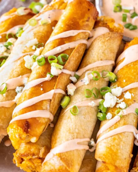 These Buffalo Chicken Taquitos are the perfect crowd-pleasing appetizer! Cheesy buffalo chicken filling is rolled up in flour tortillas and baked until crispy. Serve with an easy buffalo ranch and sprinkled with green onions and blue cheese crumbles! #buffalochicken #taquitos #appetizer #partyfood