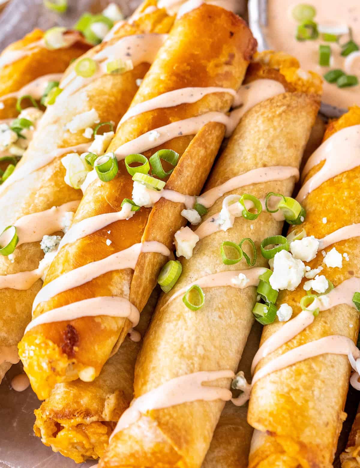 These Buffalo Chicken Taquitos are the perfect crowd-pleasing appetizer! Cheesy buffalo chicken filling is rolled up in flour tortillas and baked until crispy. Serve with an easy buffalo ranch and sprinkled with green onions and blue cheese crumbles! #buffalochicken #taquitos #appetizer #partyfood