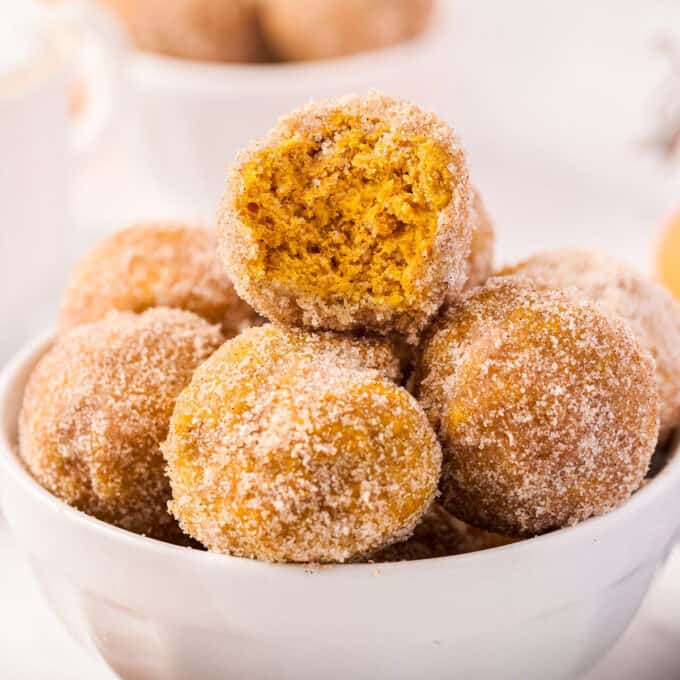 pile of pumpkin donut holes in bowl with a bite taken out of one of them