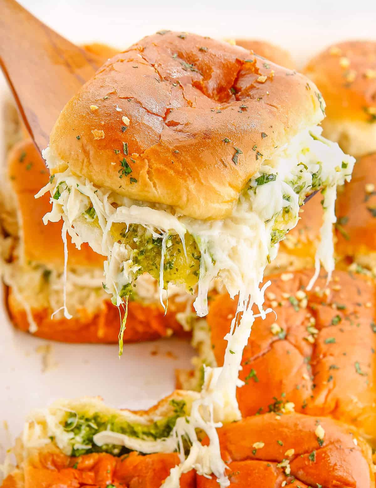 These Cheesy Garlic Pesto Chicken Sliders are gooey, hot, and so easy to make. Made with just 7 simple ingredients, with make ahead and freezer directions, they're the ultimate delicious party food! #sliders #pesto #chicken