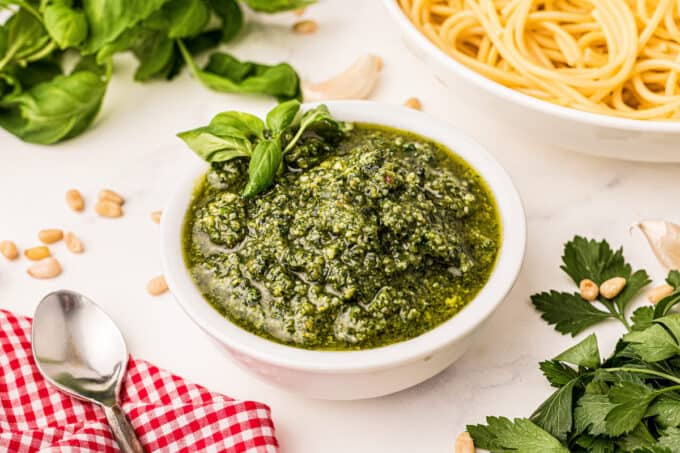 white bowl of pesto with pasta in a bowl nearby