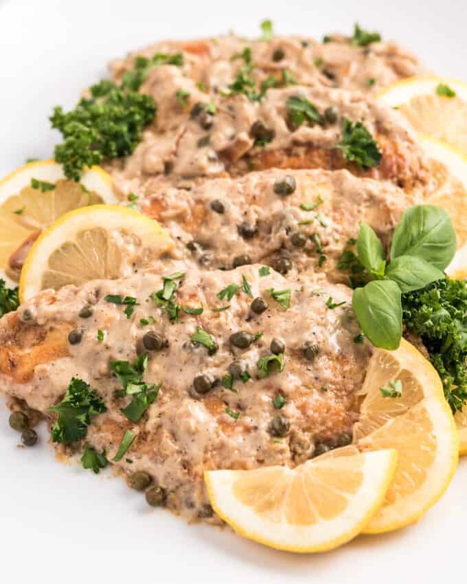 chicken piccata on white plate with lemon wedges