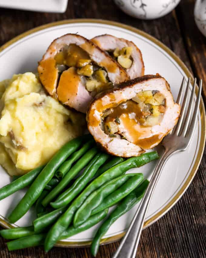 slices of stuffed pork tenderloin on white plate with green beans and mashed potatoes