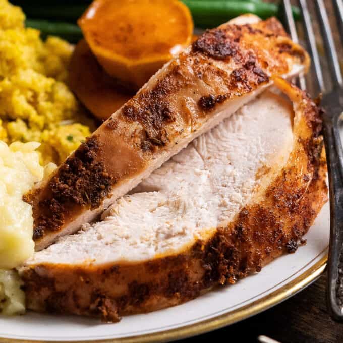 two slices of slow cooker turkey breast on plate with thanksgiving sides