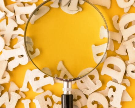 magnifying glass looking at letters on yellow background