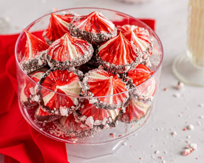 Crunchy and light meringue cookies are flavored with a hint of sweet peppermint, and swirled with red coloring. They are dipped in smooth chocolate and then sprinkled with peppermint pieces for flavor and crunch. #meringue #cookies #peppermint #baking