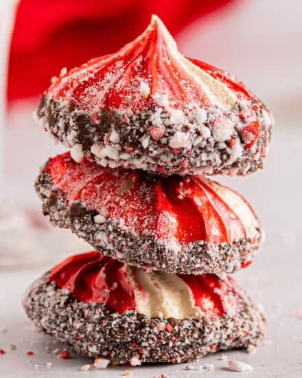 Crunchy and light meringue cookies are flavored with a hint of sweet peppermint, and swirled with red coloring. They are dipped in smooth chocolate and then sprinkled with peppermint pieces for flavor and crunch. #meringue #cookies #peppermint #baking