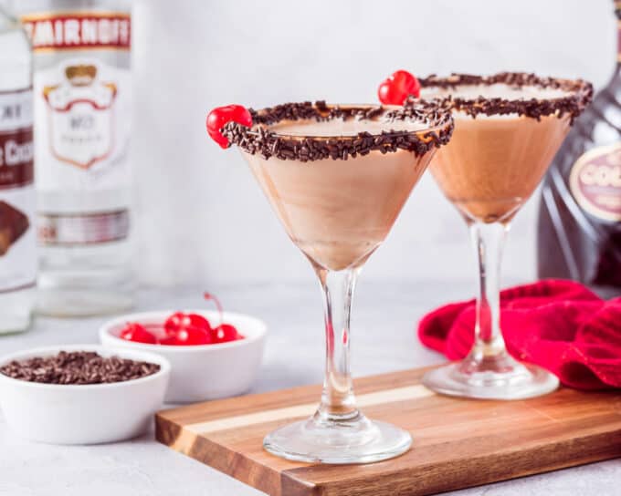 two martini glasses filled with chocolate martinis on a wooden cutting board