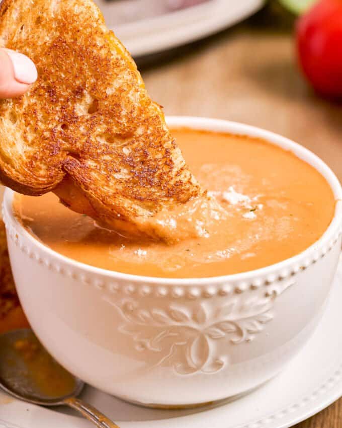 dipping a grilled cheese sandwich into a bowl of creamy tomato soup