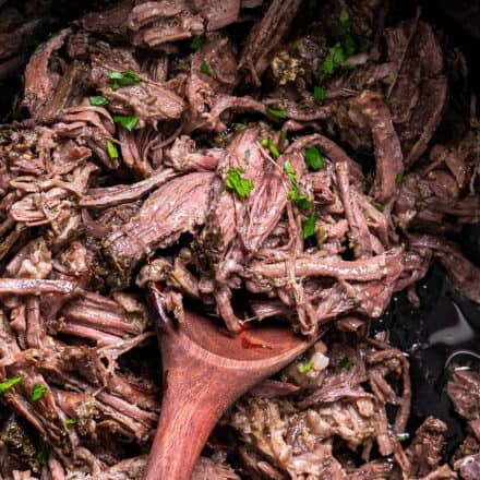 shredded mississippi pot roast in slow cooker with wooden spoon