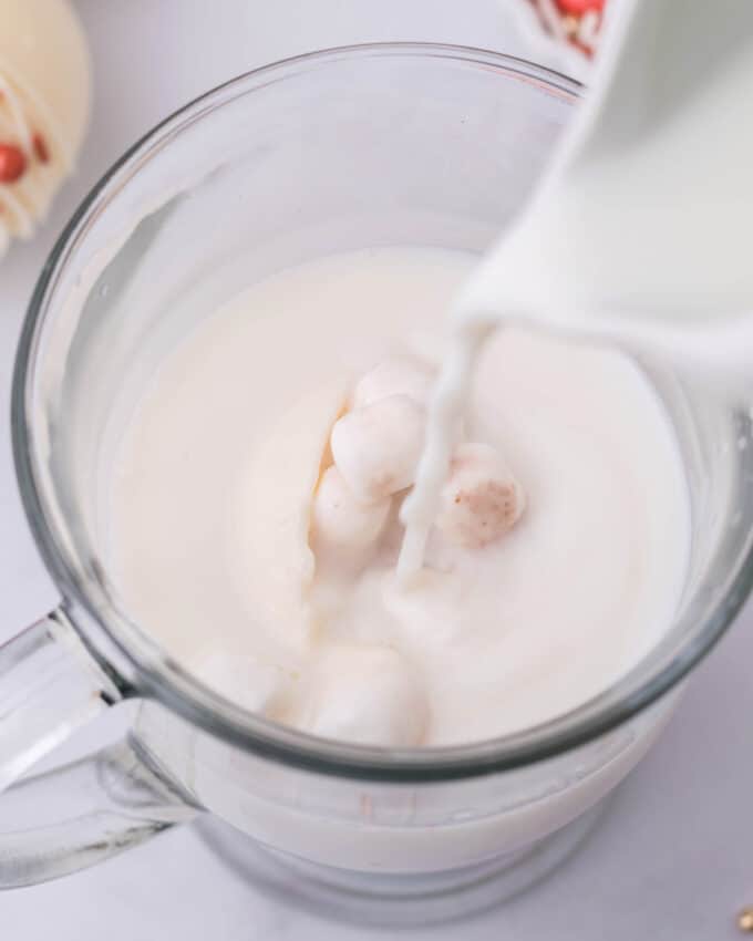 pouring hot milk onto hot cocoa bomb in glass mug