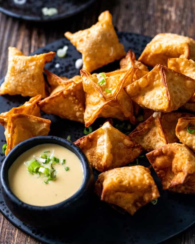 pile of crab rangoon on black plate with mustard sauce
