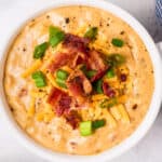 beer cheese soup in white bowl topped with bacon and green onions