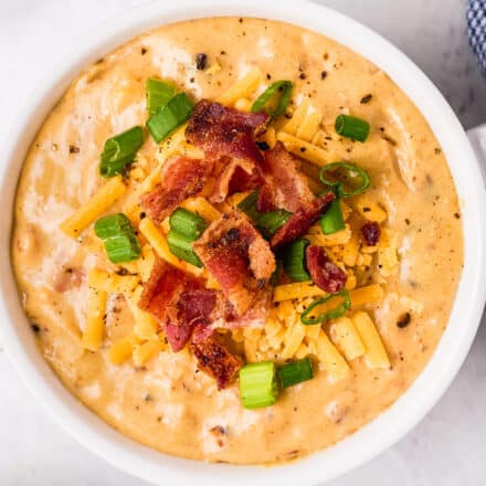 beer cheese soup in white bowl topped with bacon and green onions