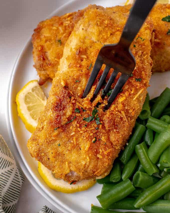 fork piercing the breading of a pork chop on a plate