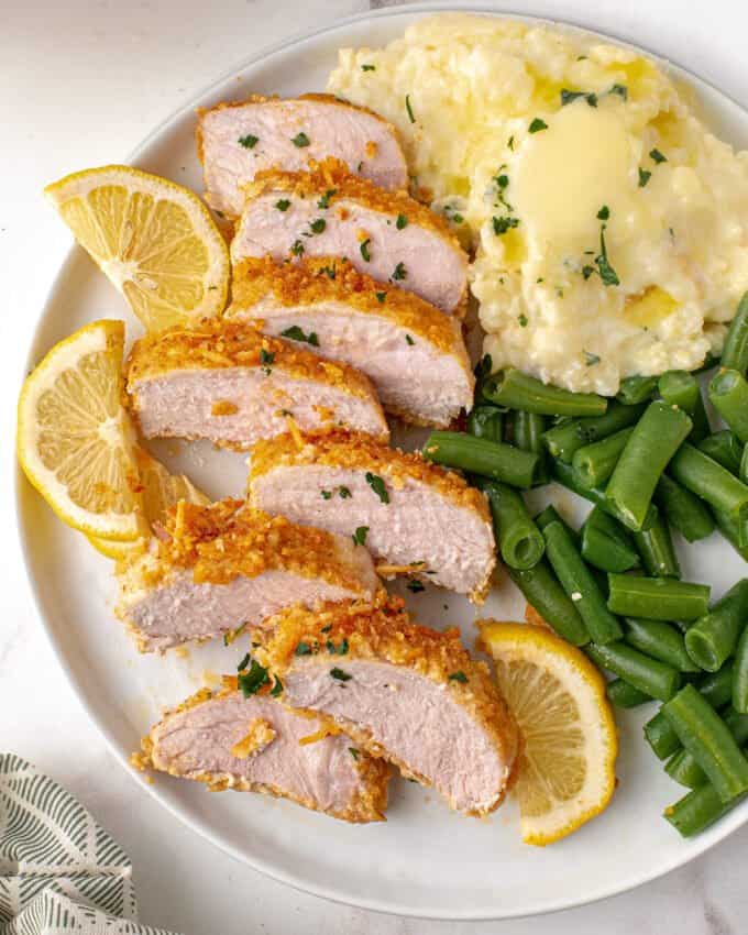 sliced baked pork chops on plate with mashed potatoes and green beans