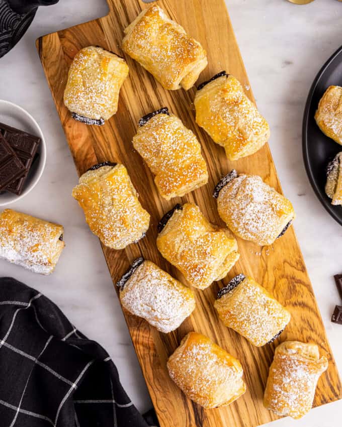 bunch of chocolate croissants on wooden board sprinkled with powdered sugar